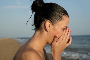 Close-up of a young woman rubbing irritated sensitive eyes on the beach, allergy reaction